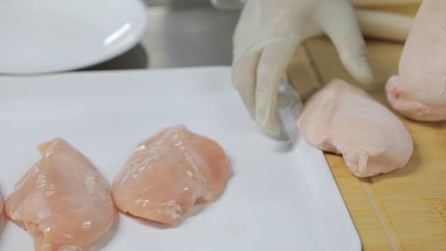 Gloved hands inspecting frozen chicken breast