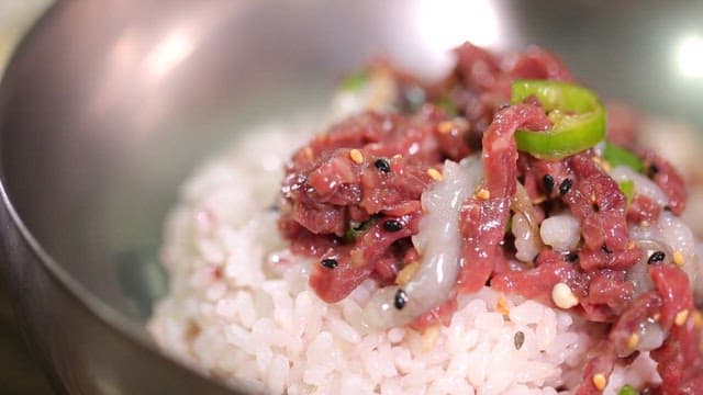 Mixing Korean beef tartare bibimbap with a spoon in a bowl