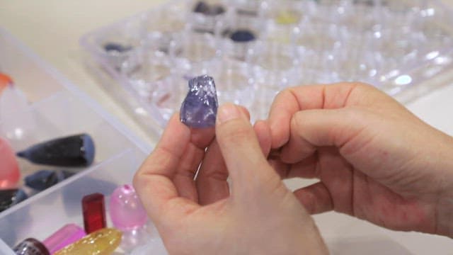 Hands holding and examining a purple gem under bright lights