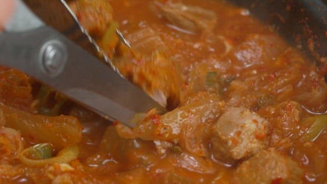 Cutting meat in kimchi stew with scissors in a pot