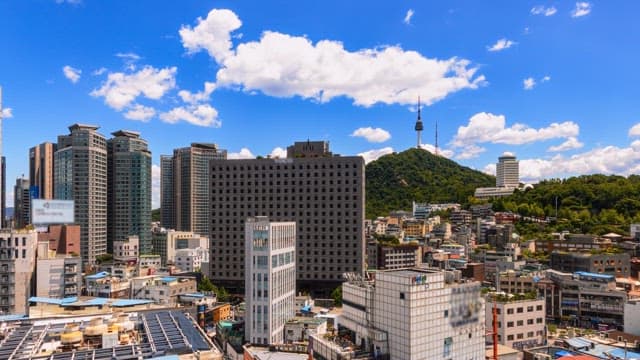 Daytime cityscape with prominent buildings and tower under cloudy sky