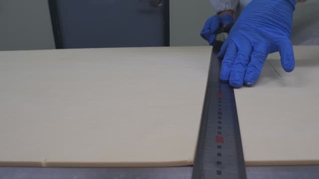 Worker in gloves cutting dough precisely with a ruler in an industrial kitchen setting
