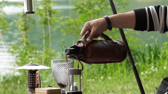 Pouring wine into a glass at an outdoor table by the lake
