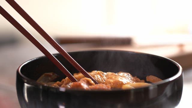 Steaming bowl of katsudon with chopsticks