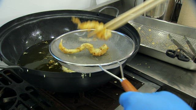 Draining fried octopus through a sieve in the kitchen