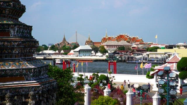 Tourists exploring a waterfront temple with passing boats on a sunny day