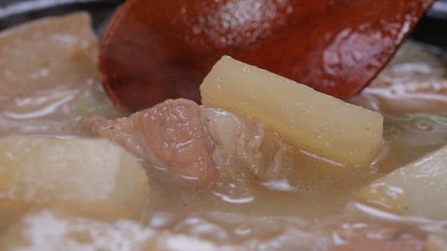 Spoonful of pork and radish soup boiling in a pot