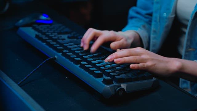 Hands typing rapidly on a backlit keyboard
