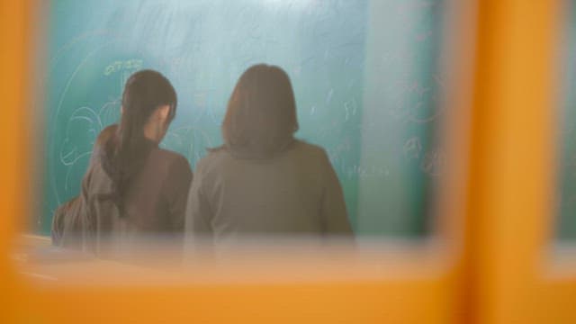 Students scribbling on the classroom blackboard viewed from outside the window