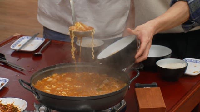 Serving steaming hot ramen into bowls at a dining table