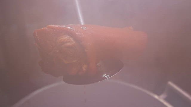 Steaming pig trotters being lifted from a pot