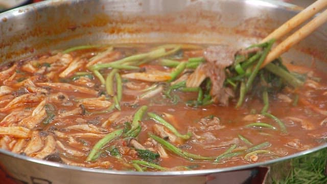 Eating hot pot with fresh water parsley and meat with chopsticks