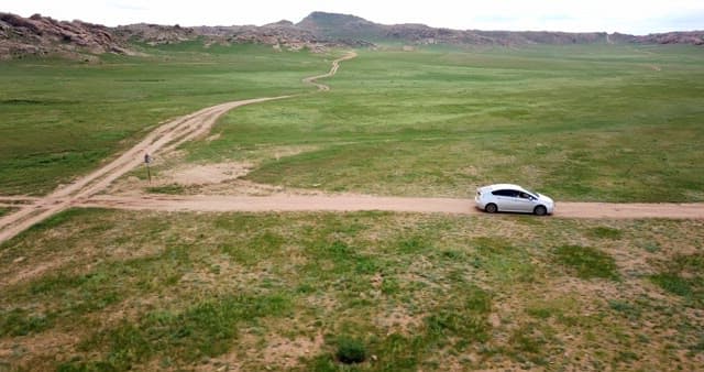 Car driving on a dirt road in a vast field