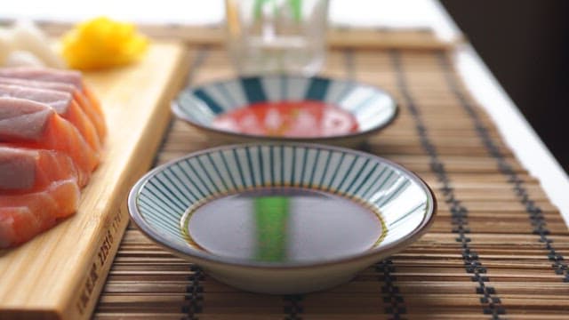 Soy sauce and red pepper sauce next to salmon sashimi on a wooden cutting board