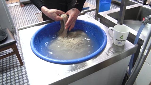 Person preparing buckwheat noodles washed in cold water in a restaurant kitchen