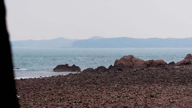 Calm rocky beach facing a serene ocean under a cloudy sky