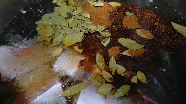 Chef adding bay leaves and spices to a cooking pot with meat