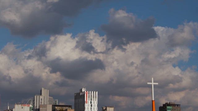 Clouds drifting over urban skyline with cross