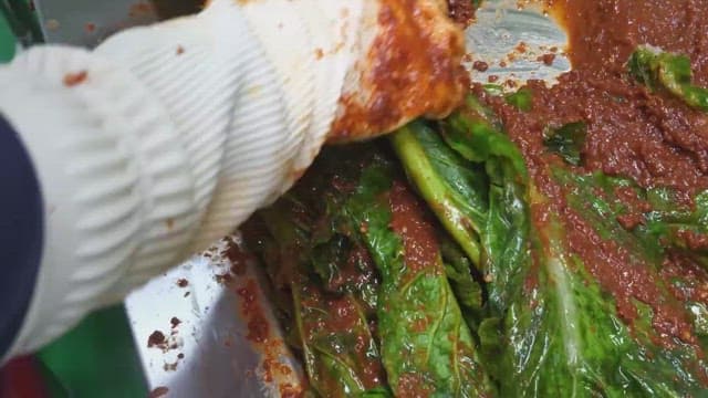 A close-up of hands kneading spicy seasoning into green vegetables using a gloved hand