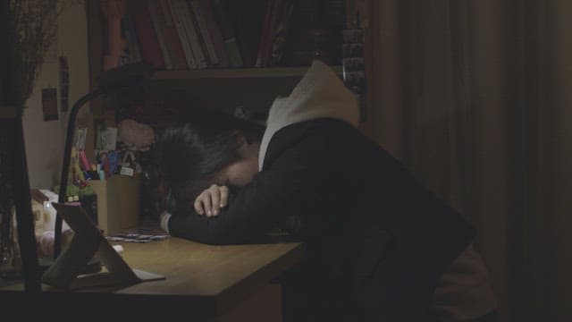 Student exhausted and sleeping on a desk in a dimly lit room