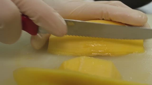 Hands slicing ripe yellow mango on white cutting board.