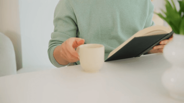 Man reading a book and drinking coffee in a bright room