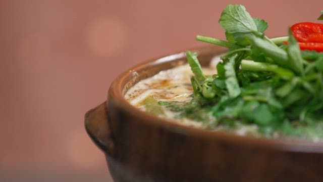 Steaming soup dish adorned with fresh water parsley and red chili