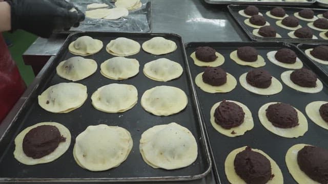 Worker preparing dough pastries filled with red bean paste in a kitchen