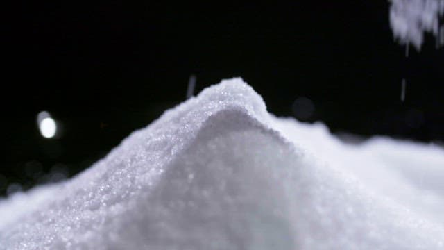Crystals of sugar pouring on a pile against black background
