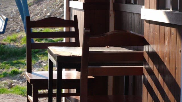 Set of wooden chairs and tables under sunlight by a wooden structure