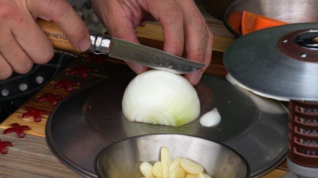 Chopping onion with a small knife on a metal plate on a wooden table
