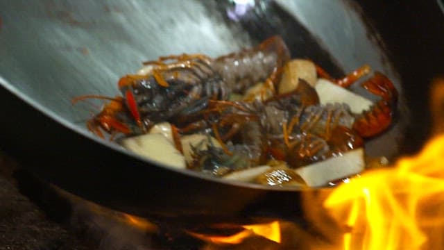 Lobsters and garlics being cooked in a pan with flames