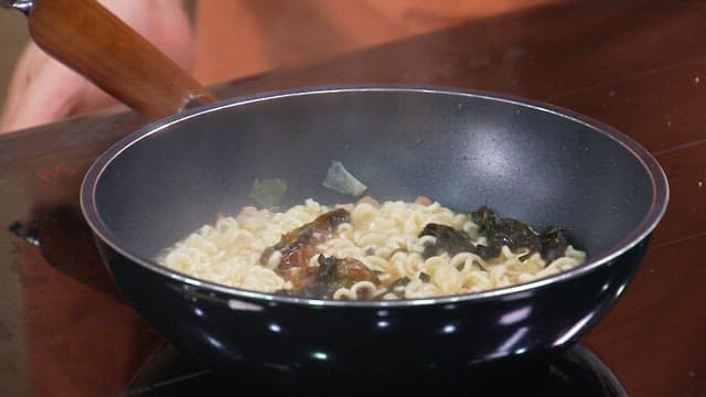 Sprinkling powder over ramen noodles boiling in a frying pan to add flavor
