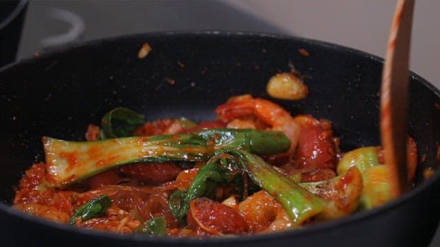Stir-frying bok choy, noodles, and shrimp in a pan