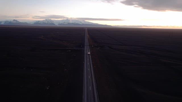 Car driving on a long road under a sunset sky