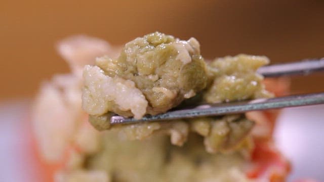 Close-up of green crab innards on chopsticks