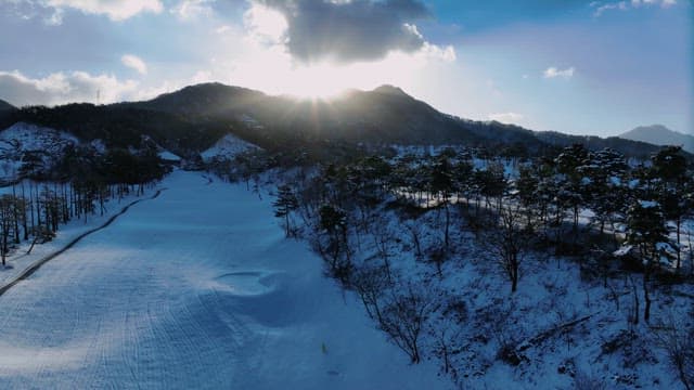 Snowy Landscape with Sun Peeking Through Mountains