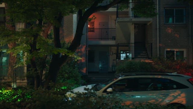 Parked car in front of an apartment building at night with dim lighting