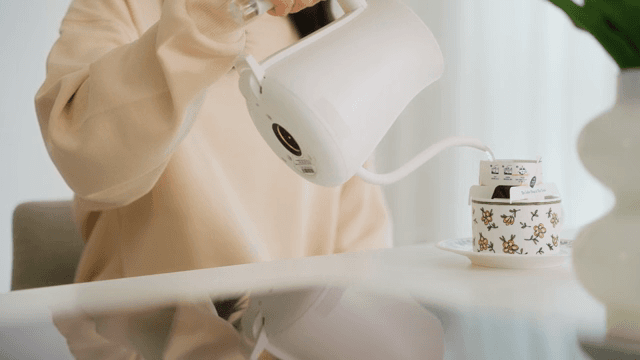 Woman pouring water into cup with coffee pot on table