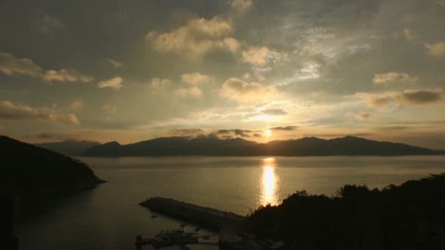 Calm ocean with mountains under the sky that changes from sunset to evening