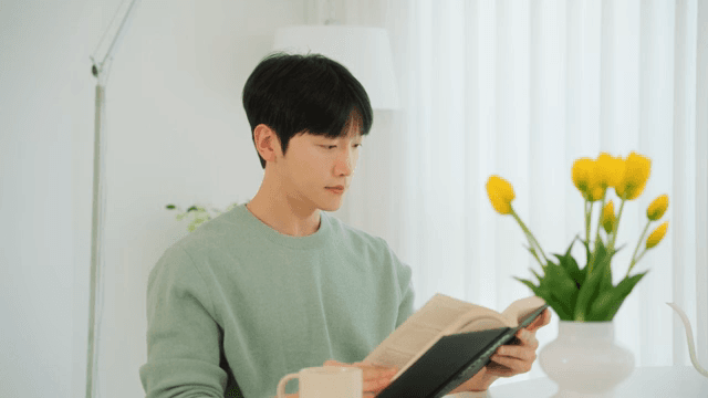 Man reading a book and drinking coffee in a bright room