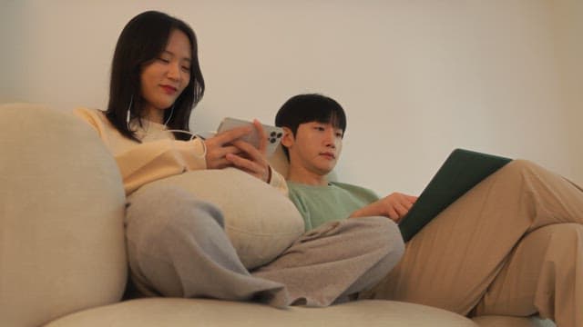 Two people using digital devices on a sofa in cozy living room