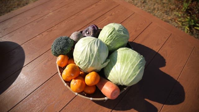 Fresh vegetables and fruits in a basket on a wooden table outdoors