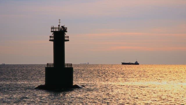 Ship and a lighthouse sailing the sea under the setting sun