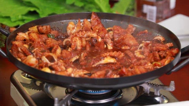 Stir-fried webfoot octopus and pork belly cooked in a pan on a gas burner