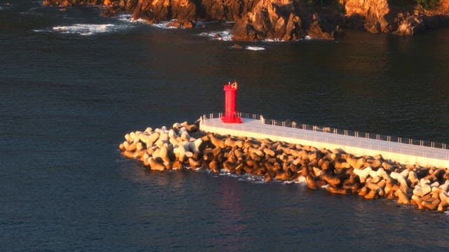 Red lighthouse on a rocky pier at sunset