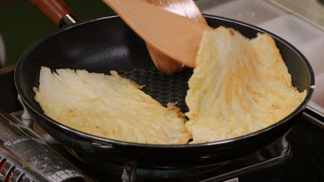 Cabbage pancakes cooked in a hot oiled pan with a wooden spatula