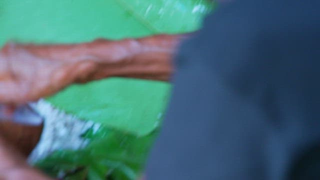 Hands grating coconut over banana leaves