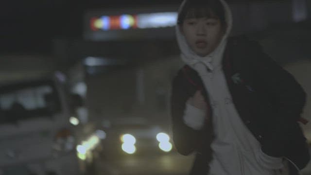 Woman wearing hoodie and jacket running at night while talking on the phone with worried expression