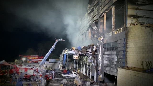 Nighttime fire at an industrial building with firefighters working to control the blaze